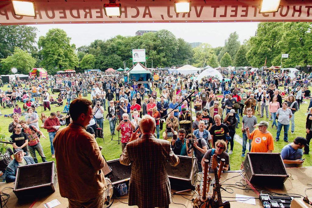 Two men performing on an outdoor stage to a large crowd