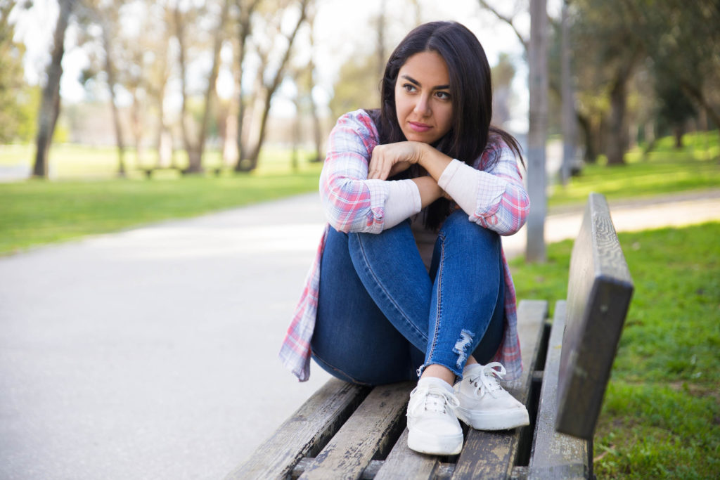 Une femme assise sur un banc de parc étreignant ses genoux à sa poitrine