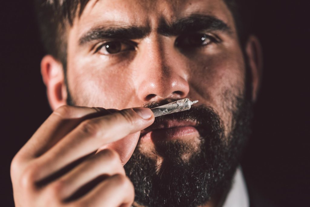 A man with a beard holding a rolled joint up to his nose