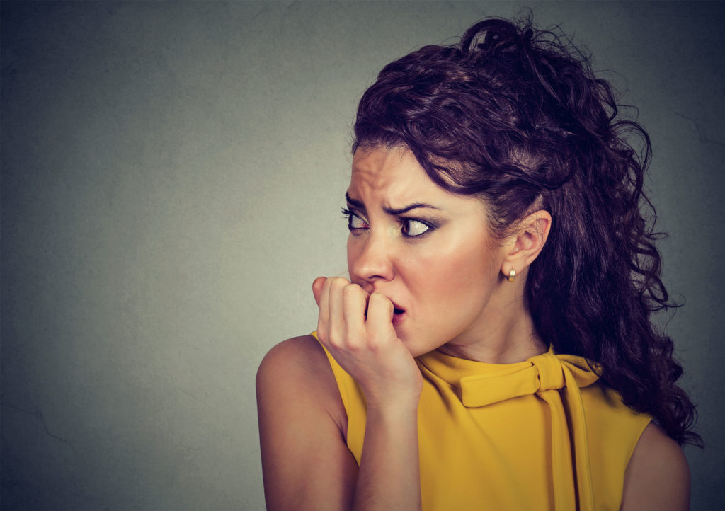 A woman looking to the side and frowning. She is biting her nails