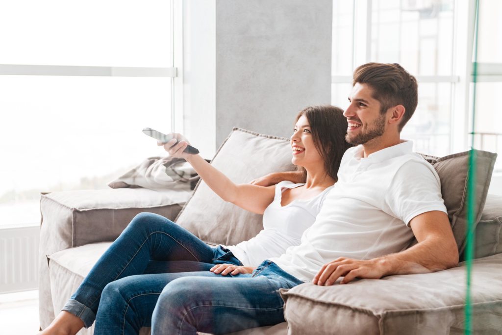 Una pareja sentada en un sofá, sonriendo y viendo la televisión.