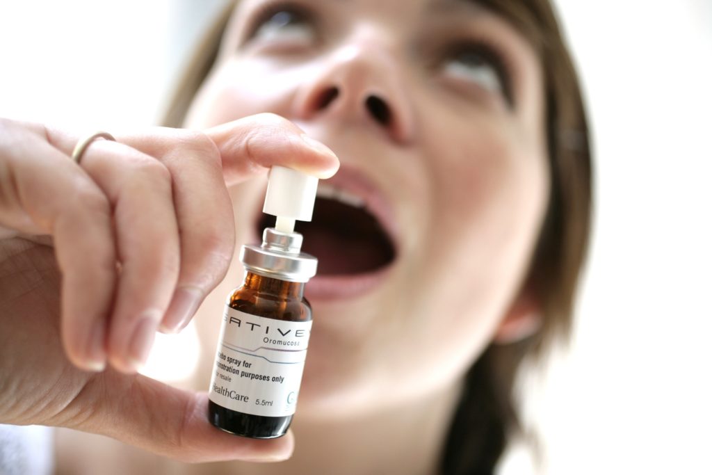 A small spray bottle of Sativex being pointed towards a person's open mouth