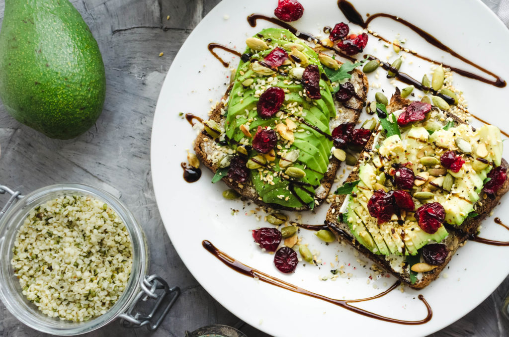 A white plate of avocado on toast with hemp seeds and dried fruit