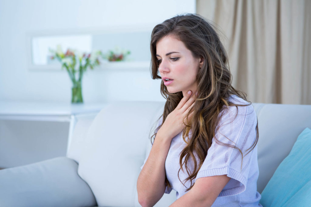 A woman sat on a sofa and holding her throat