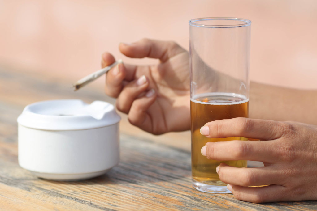 A woman smoking a join and holding a glass of beer