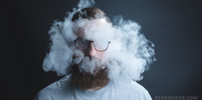 Un hombre con barba y vasos rodeados de humo de cannabis.