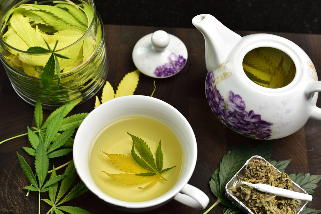 Una olla de té blanco y púrpura y una taza de té llena de hojas de cannabis.