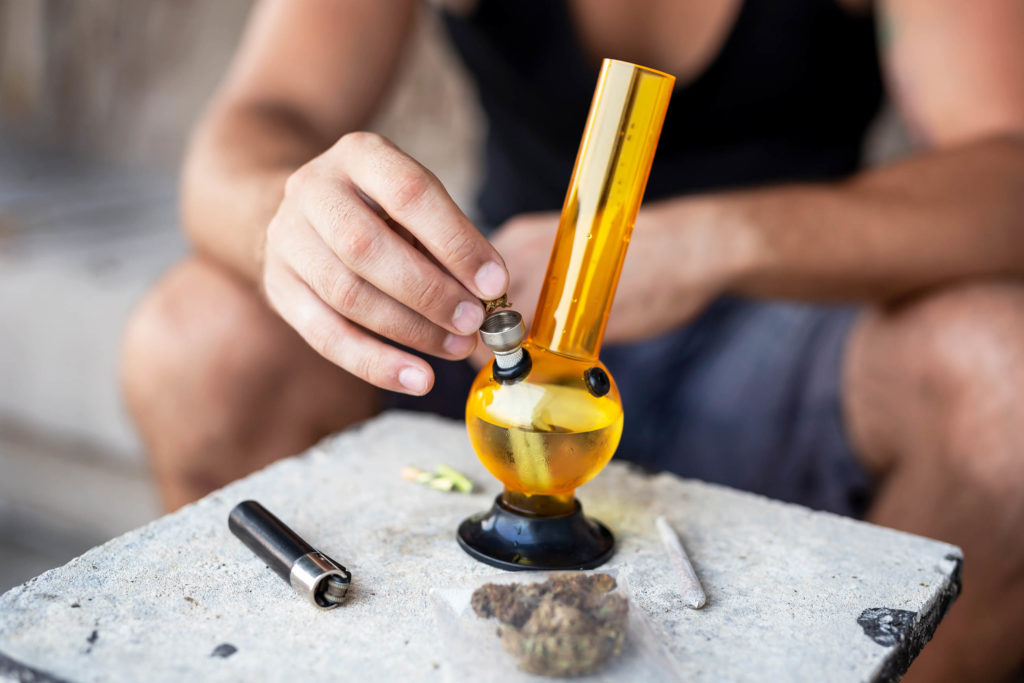 A person placing a piece of herbal cannabis in an orange bong