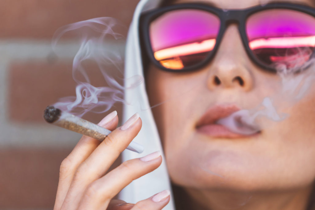 A woman wearing sunlasses with pink lens smoking a joint