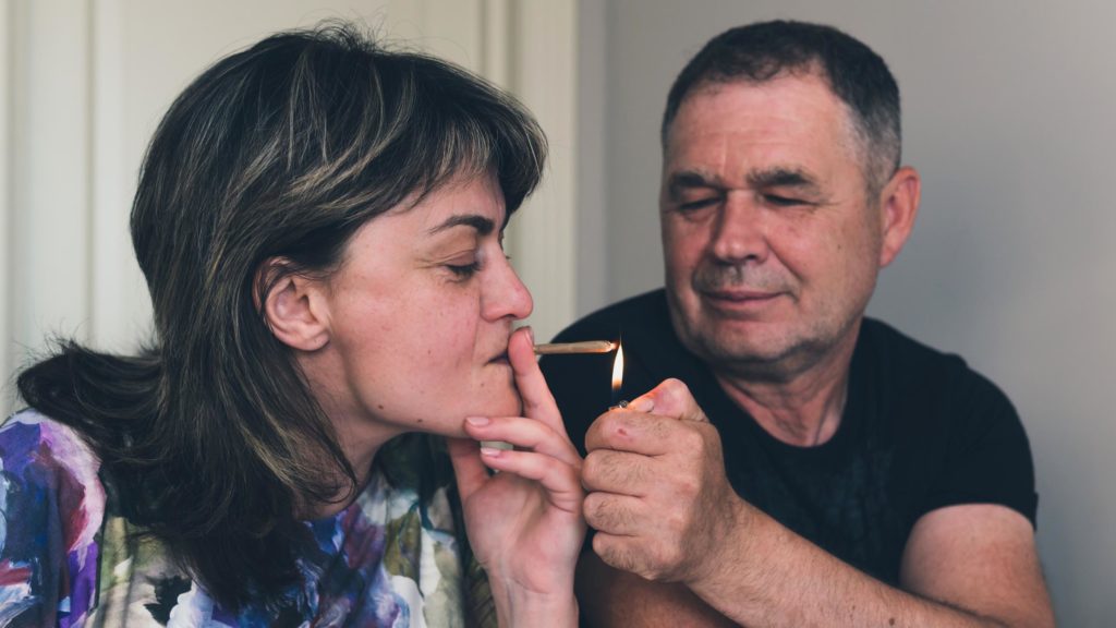 A woman smoking a joint and a man lighting it for her