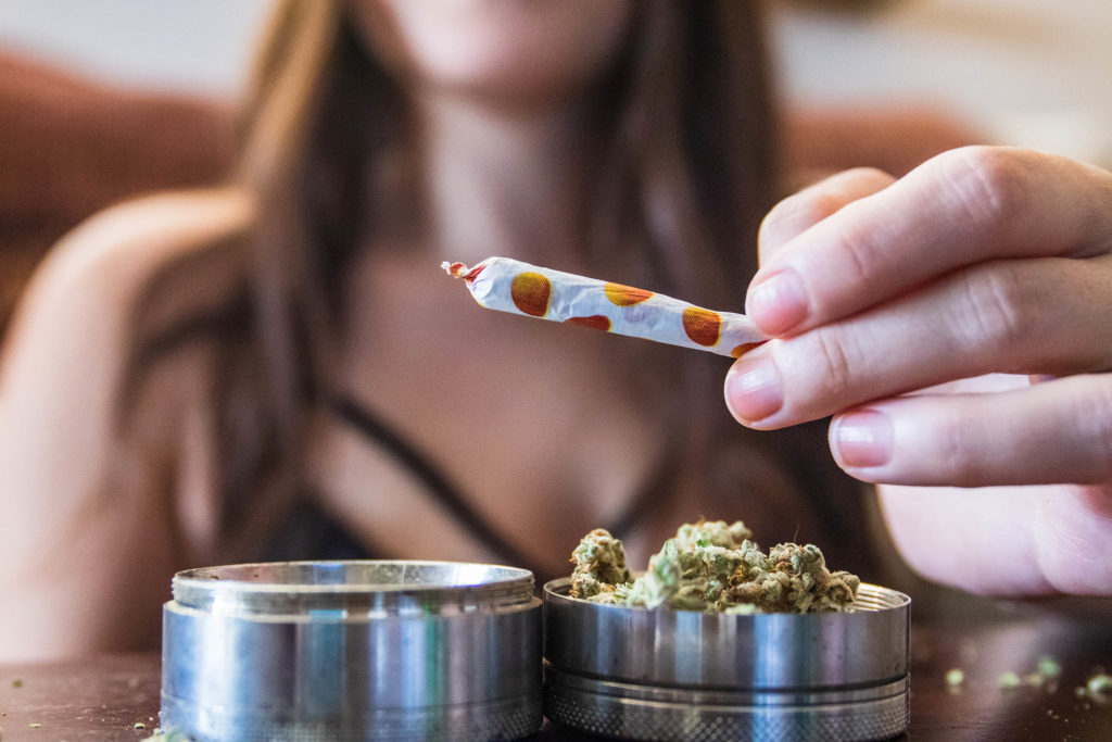 A woman holding up a rolled joint with orange spots on it