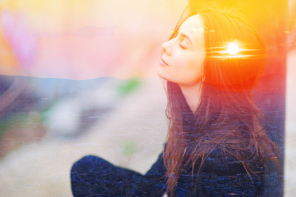 A woman sat cross-legged with her eyes shut. In the background is a sunset