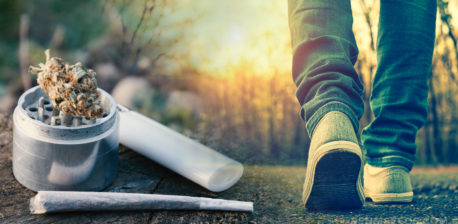 A person walking outdoors, a grinder with cannabis bud, joint and lighter