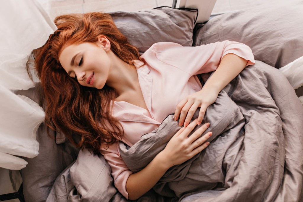 Redhead sleeping in a bed with a smile on her face