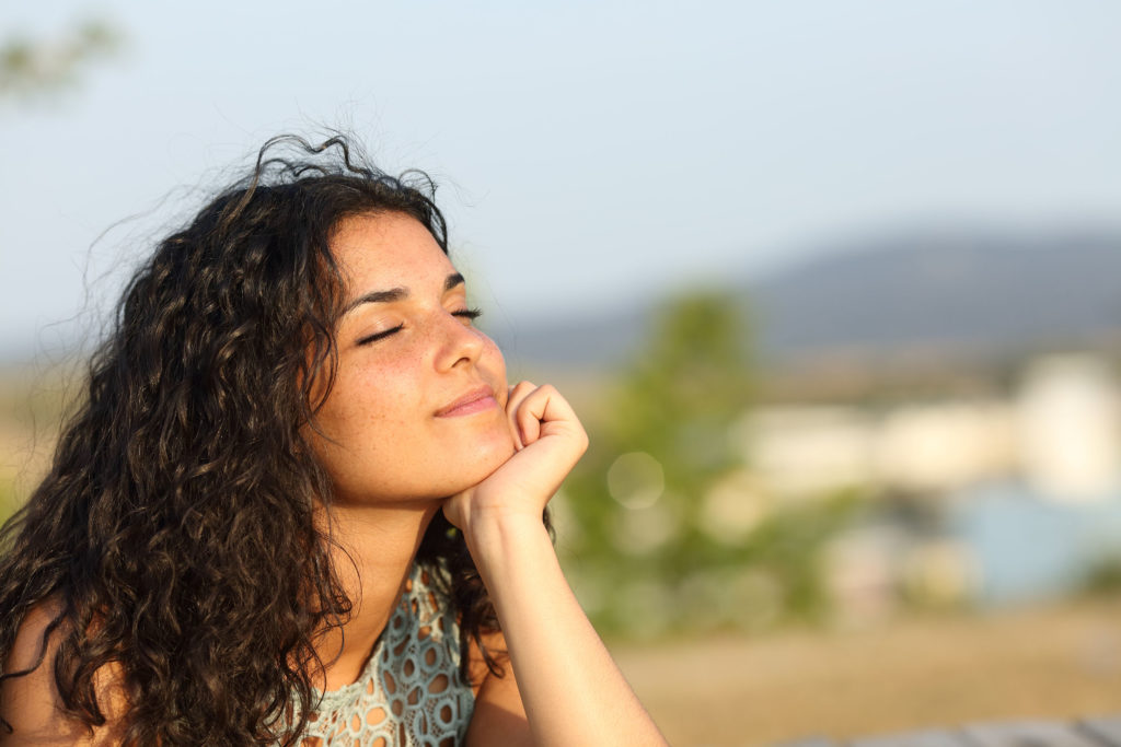 Une femme souriante avec ses yeux fermés, pose son menton sur sa main