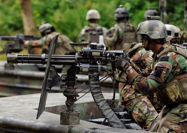 A soldier wearing camouflage and a helmet pointing a large machine gun