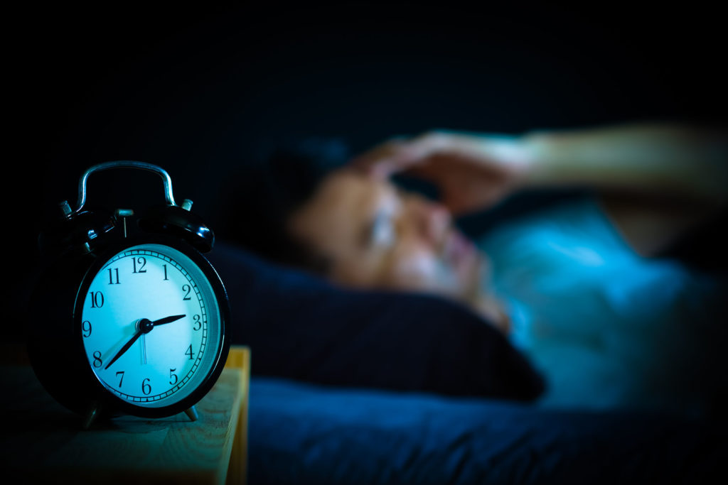 Un homme avec une insomnie reposant dans un lit avec une horloge à côté