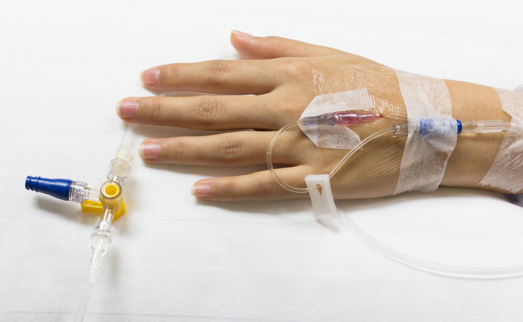 A person with cannula in a hand on a white bed sheet