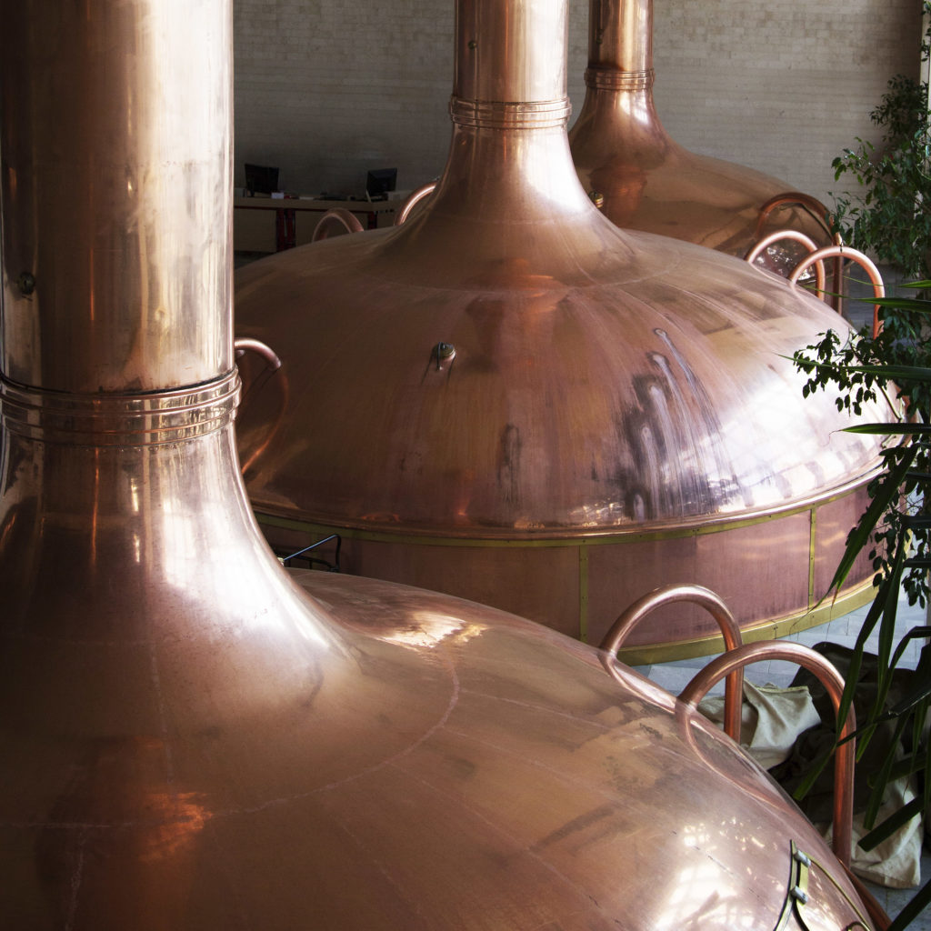 Tres teteras de cobre grandes dentro de una cervecería.