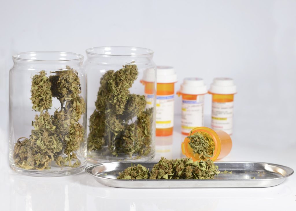 Two glass jars full of cannabis buds and four orange medical containers