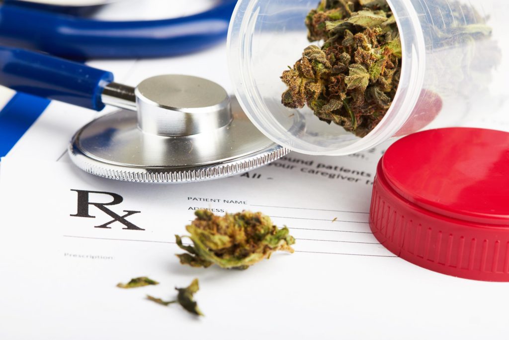 Cannabis buds in a plastic container, a stethoscope and a medical form