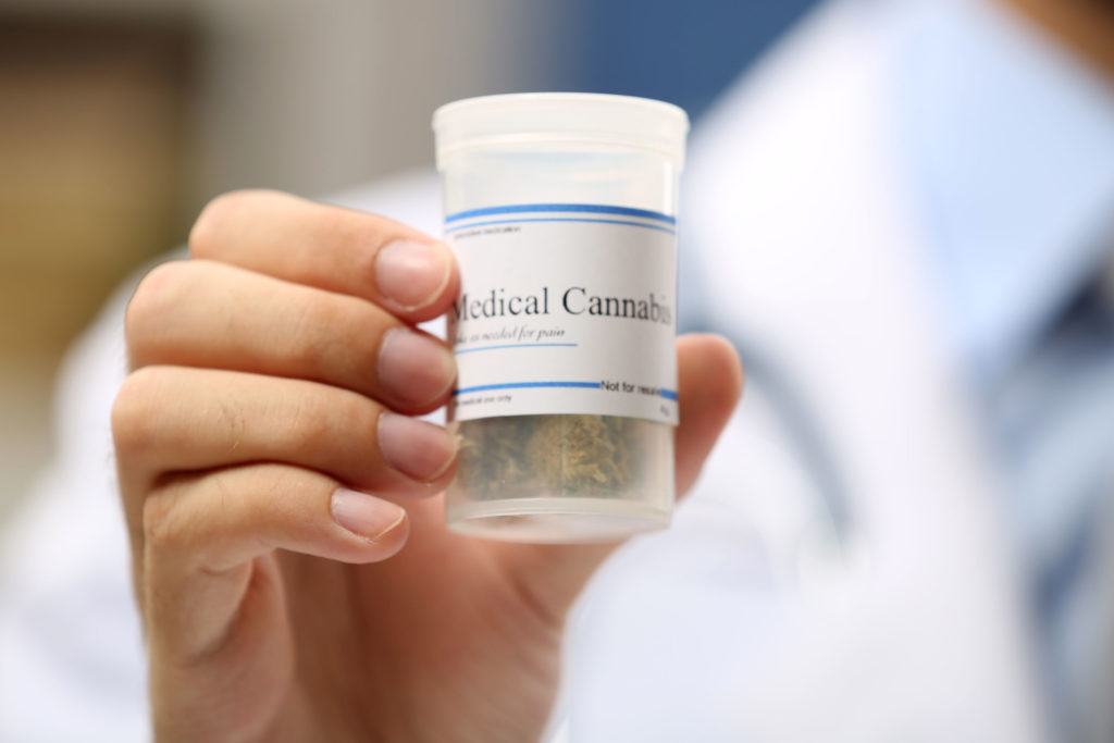 A hand holding up a small plastic container labelled Medical Cannabis