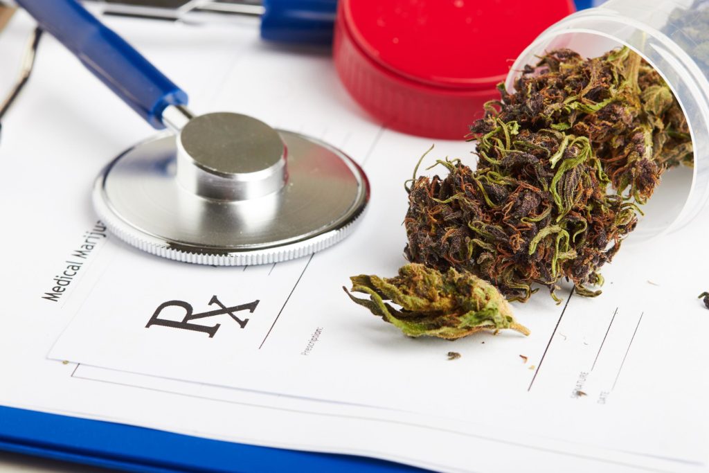 Buds de cannabis en un recipiente de plástico, una forma médica y un estetoscopio