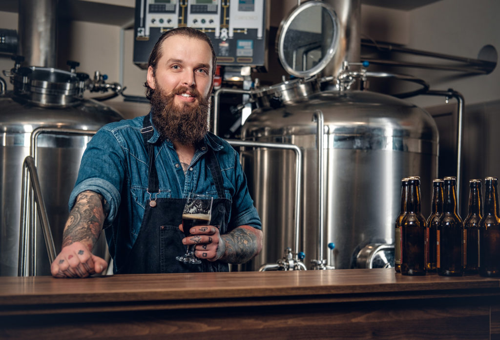 Ein Barkeeper, der eine Schürze trägt und ein Glas Bier hält