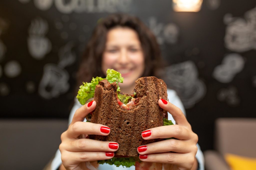 Una mujer sosteniendo un sándwich de pan de trigo integral.