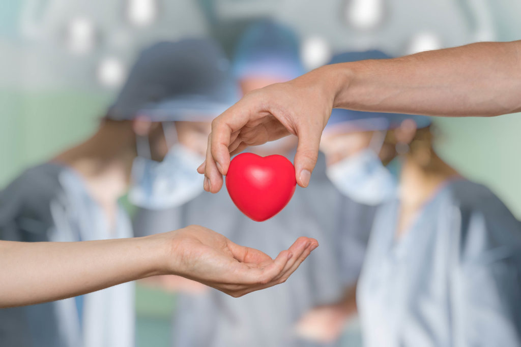 Someone passing a red heart to another person. In the background are three surgeons