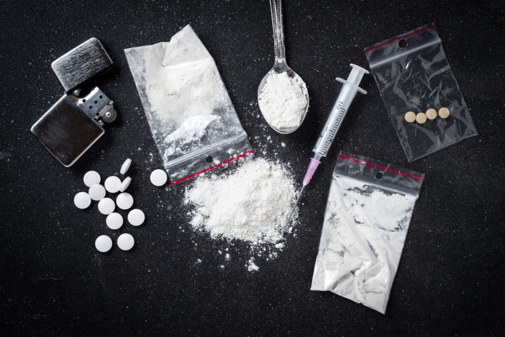 Taschen mit Heroin, Tabletten, Löffel, Feuerzeug und Impfstoffe mit Nadeln auf einer schwarzen Oberfläche