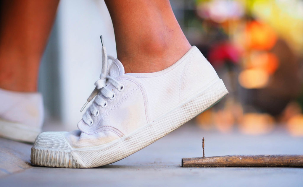 A person wearing white trainers about to step onto a rusty nail