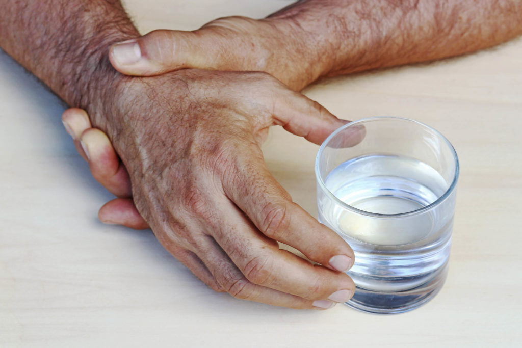 Een man die zijn hand vasthoudt en probeert een glas met de andere hand vast te houden