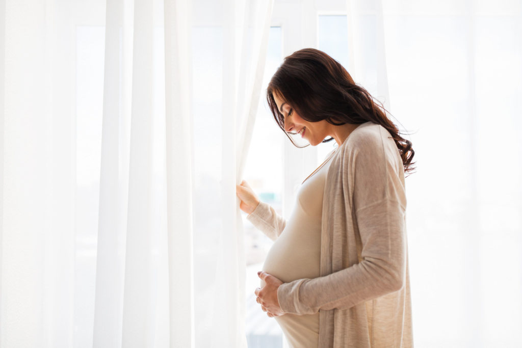 Une femme enceinte tenant son estomac à côté d'une fenêtre