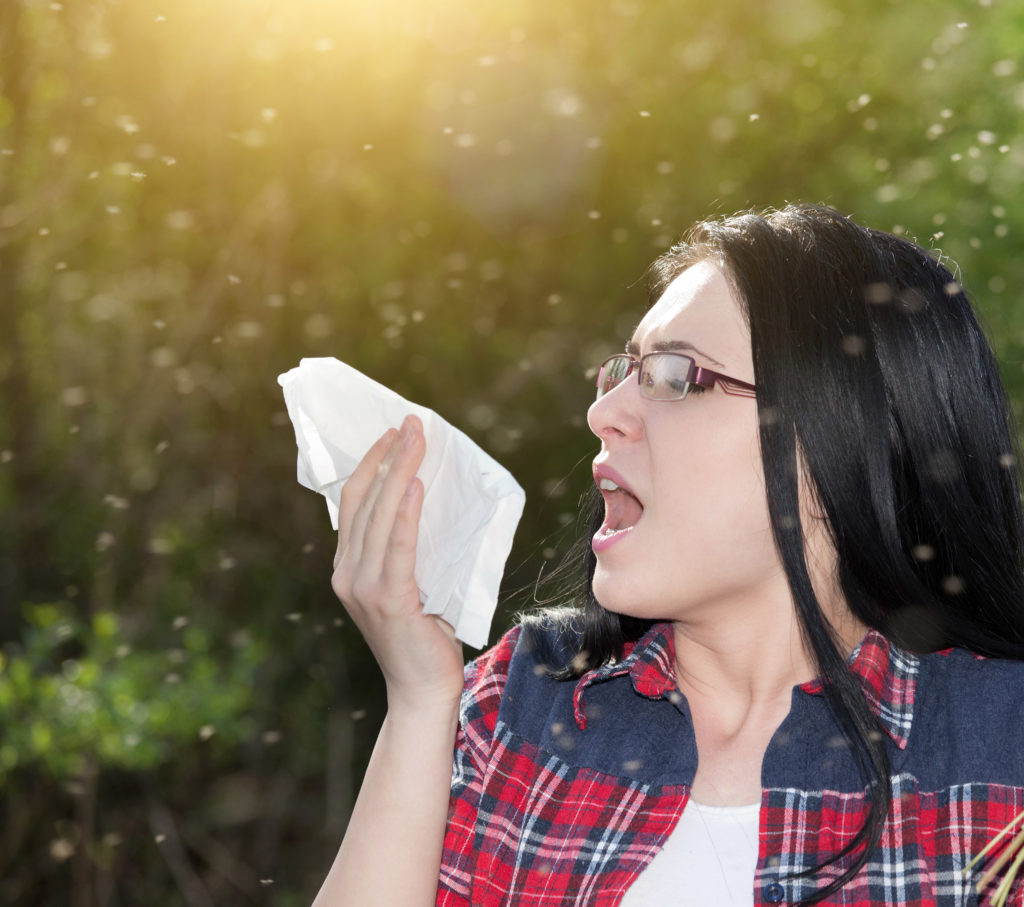 A woman standing outside and sneezing into a tissue