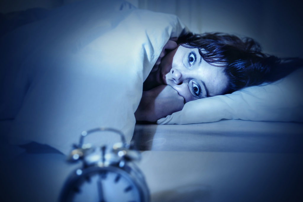 Una mujer con insomnio acostado en una cama mirando un reloj