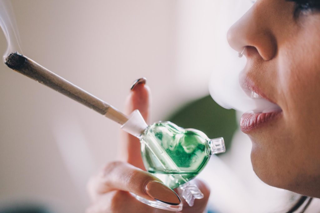 A woman with a septum piercing smoking a joint through a pipe