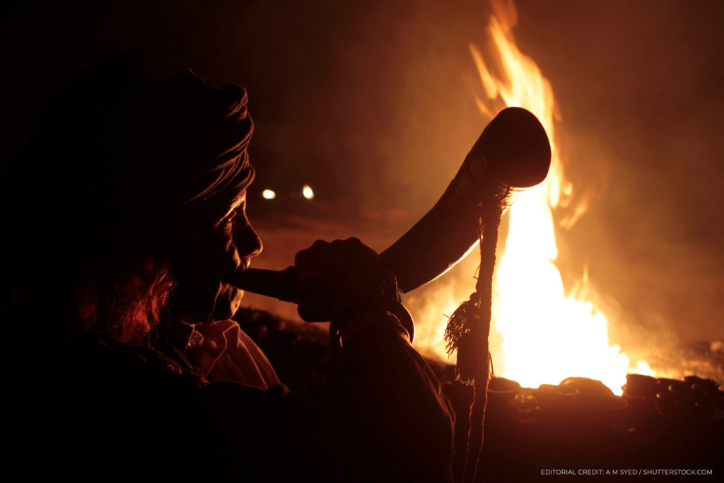 A person blowing a horn in front of a campfire