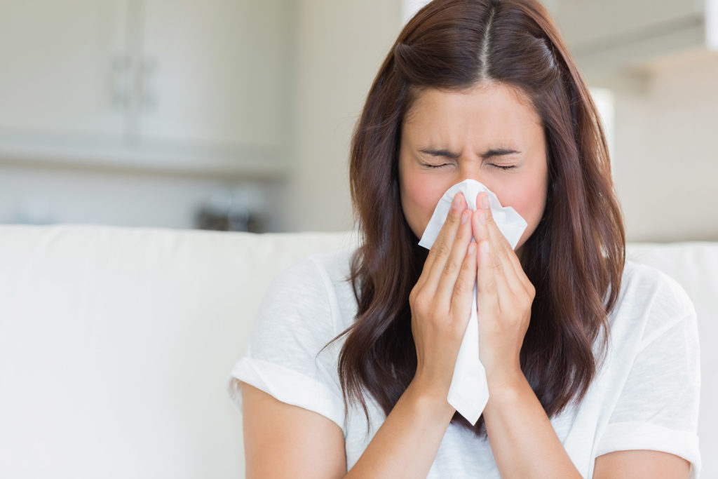 A woman with brown hair blowing her nose into a tissue