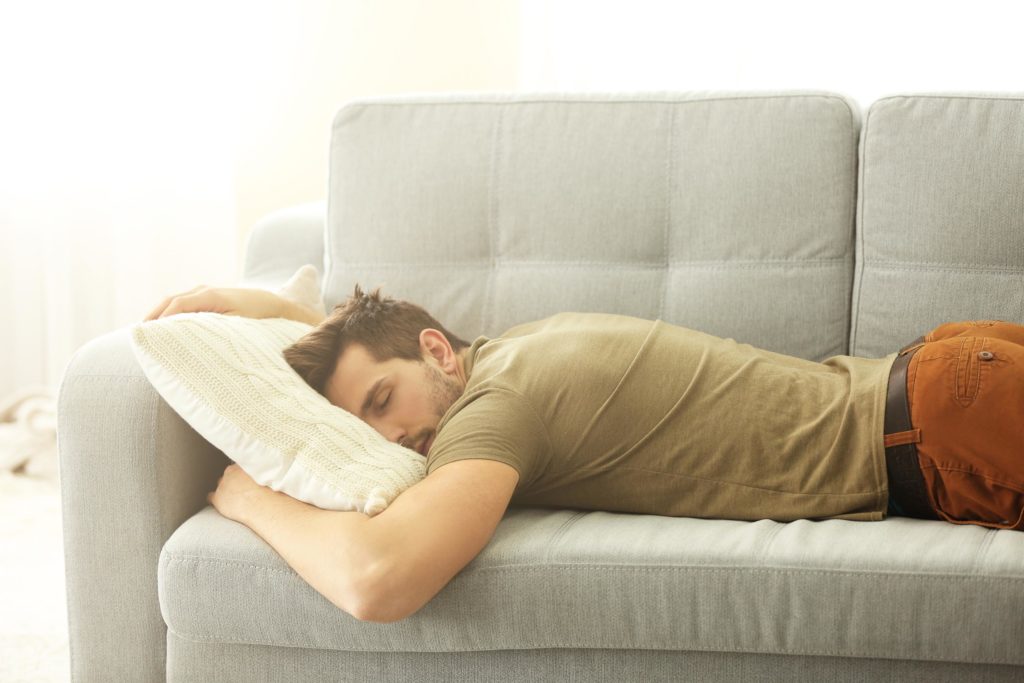 Un hombre durmiendo en el sofá con una almohada.