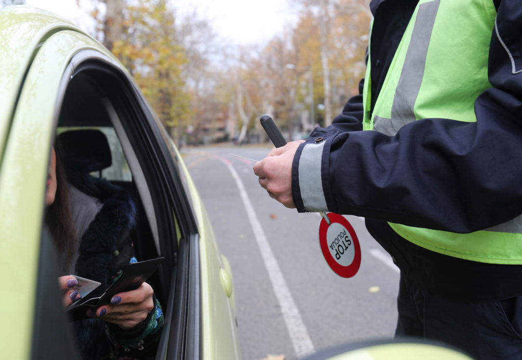 A policeman standing next to the window of a car talking to the driver