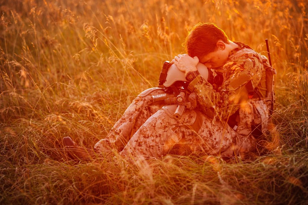 Een soldaat zat op een veld en rustte zijn hoofd op zijn helm