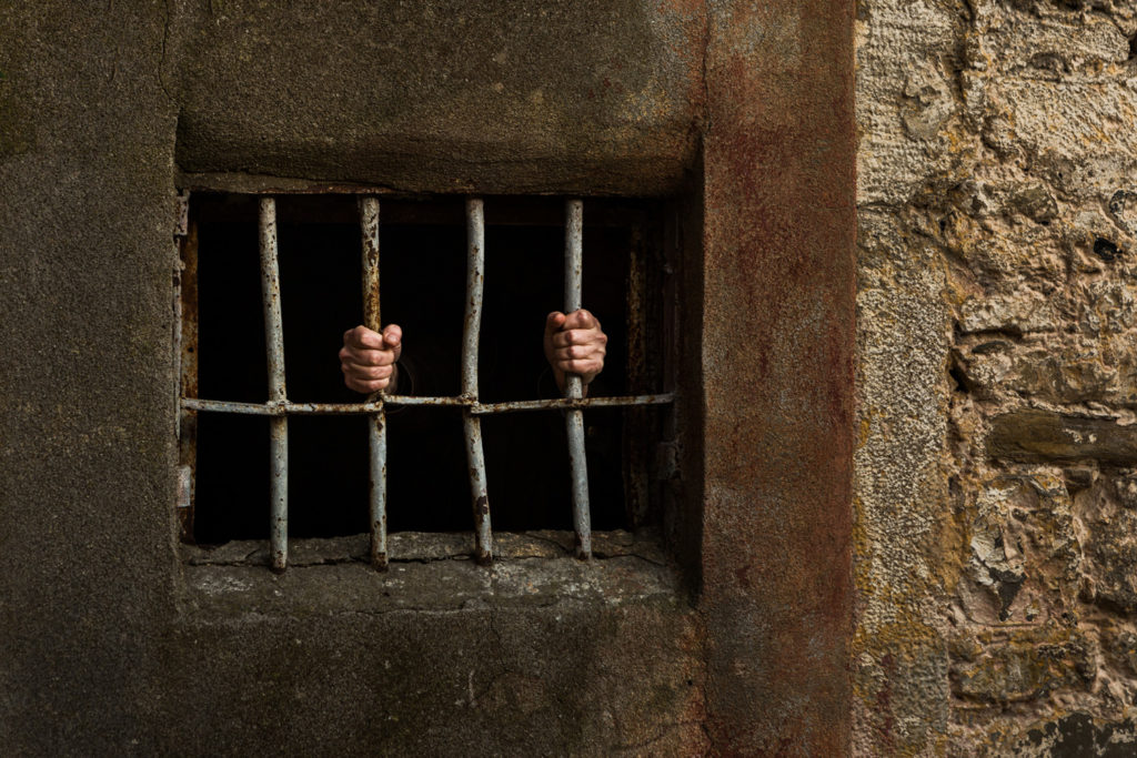 A person in a jail holding the bars of the cell