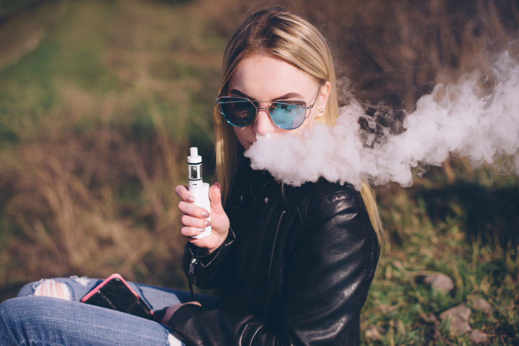 Een vrouw met zonnebril rokende e-vloeistof van verdamper