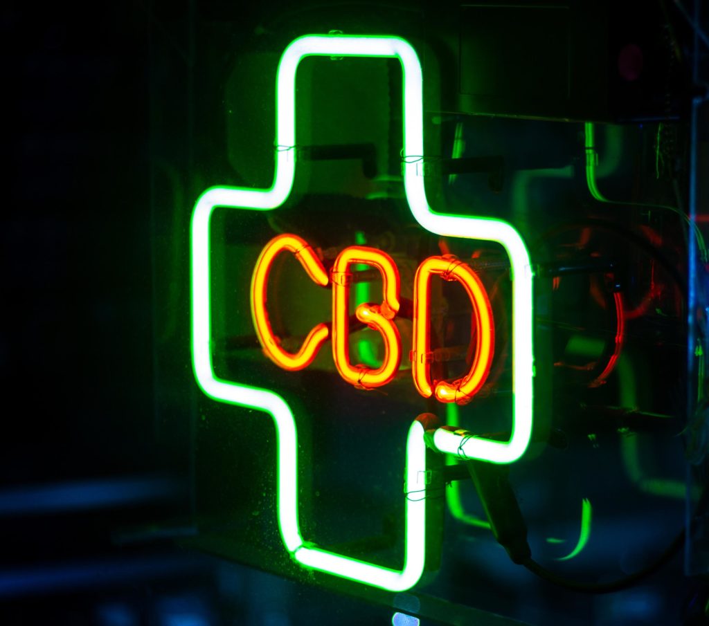 A green neon plus sign with CBD in the middle in red