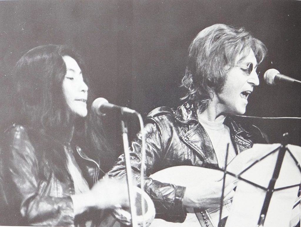 Una foto en blanco y negro de Yoko Ono y John Lennon cantando.