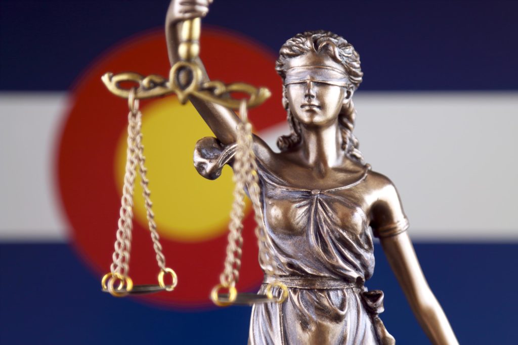 The Colorado flag and a bronze statue holding balancing scales 