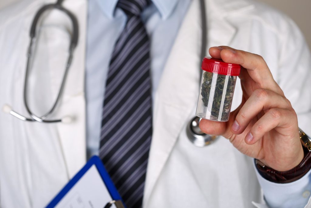 A doctor with a stethoscope around his neck holding a plastic pot of cannabis