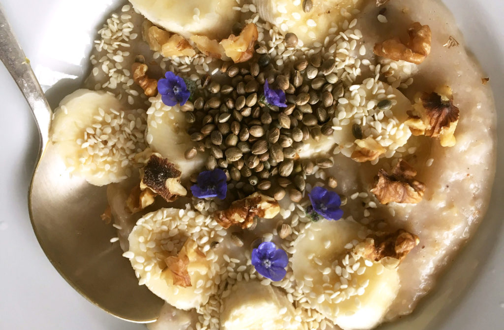 Hemp seed porridge with banana, sesame seeds, walnuts, edible flowers and a spoon beside