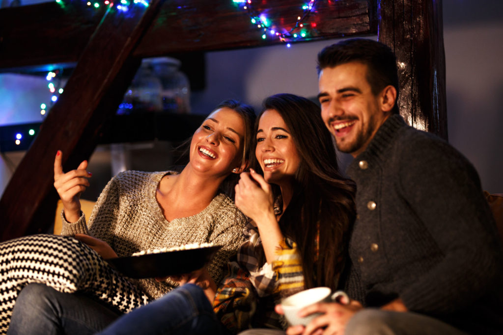 People laughing and watching a movie with a bowl of popcorns